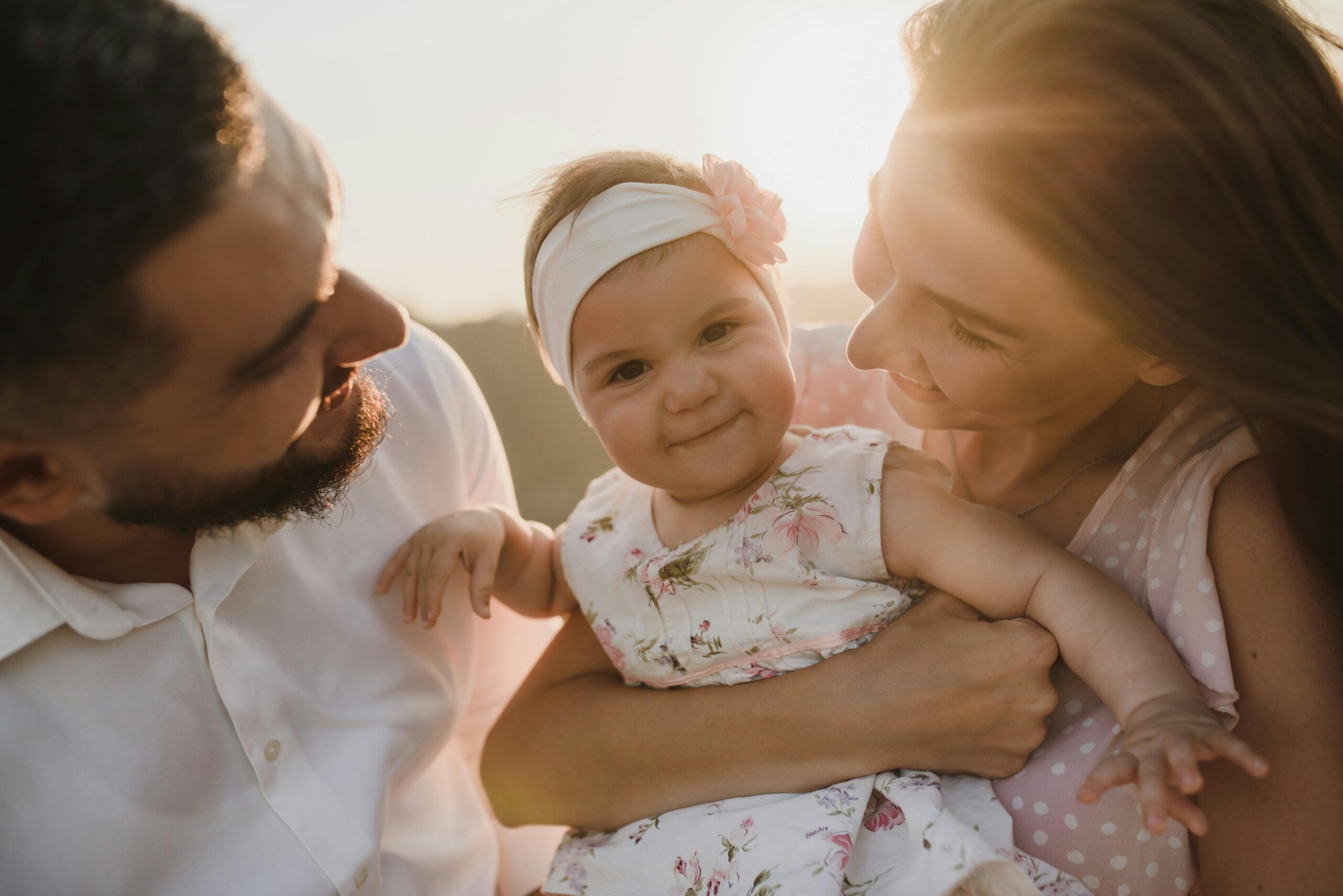 A joyful family scene with parents holding their smiling baby at sunset.